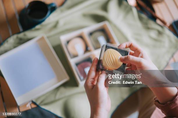 high angle view directly above asian chinese woman hand holding snow skin mooncake she received from her friend gift box in living room - care package stock pictures, royalty-free photos & images