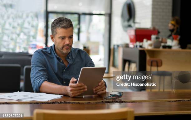business man working at a cafe on his tablet while waiting for a coffee - business studies stockfoto's en -beelden