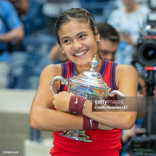 Tennis champion Emma Raducanu hugging her trophy in disbelief after defeating Leylah Fernandez in the women's finals and receiving $2.5 million at...
