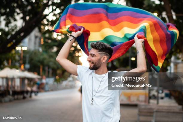 giovane gay tiene bandiera arcobaleno - gay pride flag foto e immagini stock