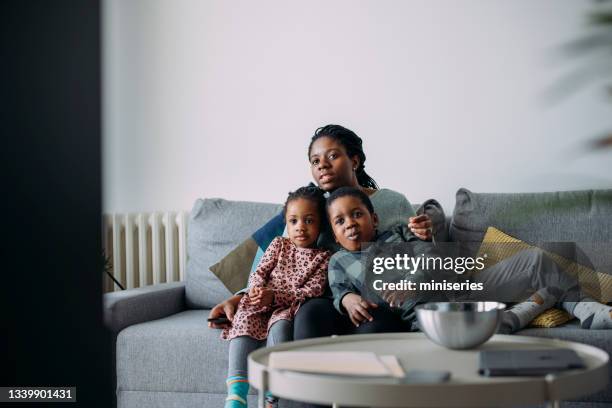 super mom: eine junge mutter und ihr junge und ein mädchen verbringen zeit miteinander zu hause und schauen fern - kid watching tv stock-fotos und bilder