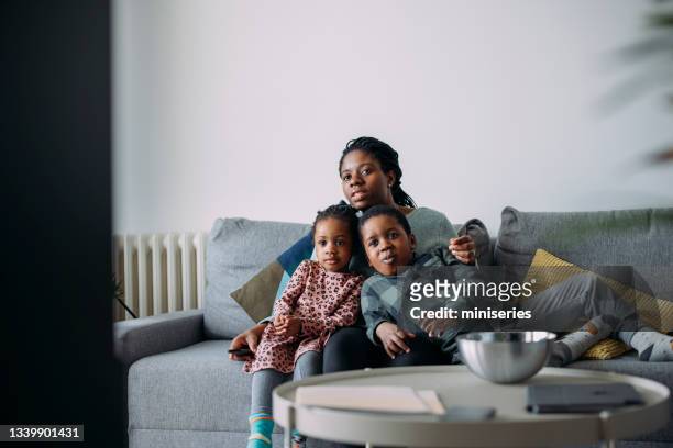 super mom: a young mother and her boy and a girl spending quality time together at home watching tv - children watch tv stockfoto's en -beelden