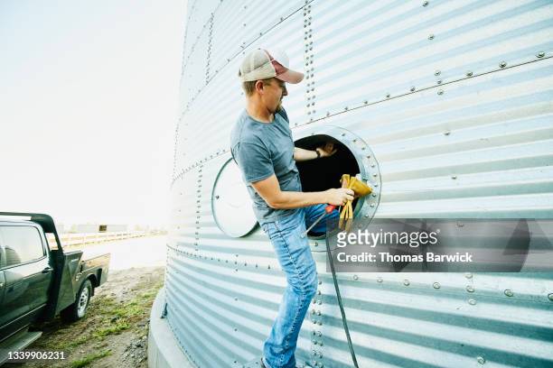 Medium wide shot of farmer climbing into silo for repair