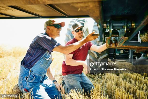 medium wide shot of farmers working on combine header in wheat field during harvest - equipos agrícolas fotografías e imágenes de stock