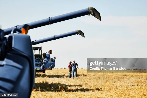 extreme wide shot of two farmers in discussion next to combines in wheat field after summer evening harvest - farm field combine fotografías e imágenes de stock