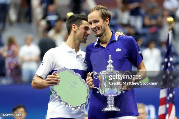 Novak Djokovic of Serbia holds the runner-up trophy and talks with Daniil Medvedev of Russia who celebrates with the championship trophy after...