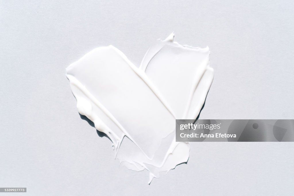 Textured smears of white cream applied on white background in heart shape. Body lotion for perfect skin. Macrophotography in flat lay style