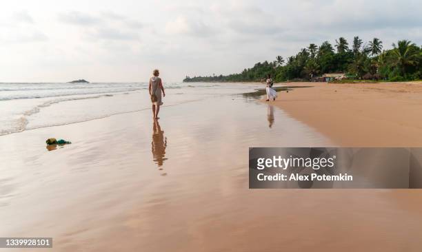 optimistic happy 50 years old woman, a european tourist, walks away on the sandy beach of the indian ocean in bentota, sri lanka, in the early evening. - 50 54 years stockfoto's en -beelden