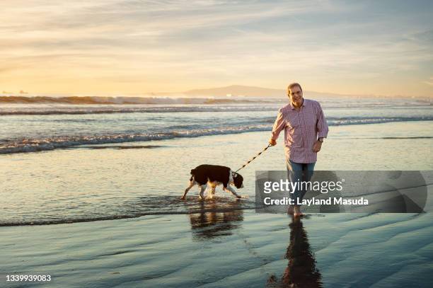 dad walks the dog on the beach - mature adult walking dog stock pictures, royalty-free photos & images