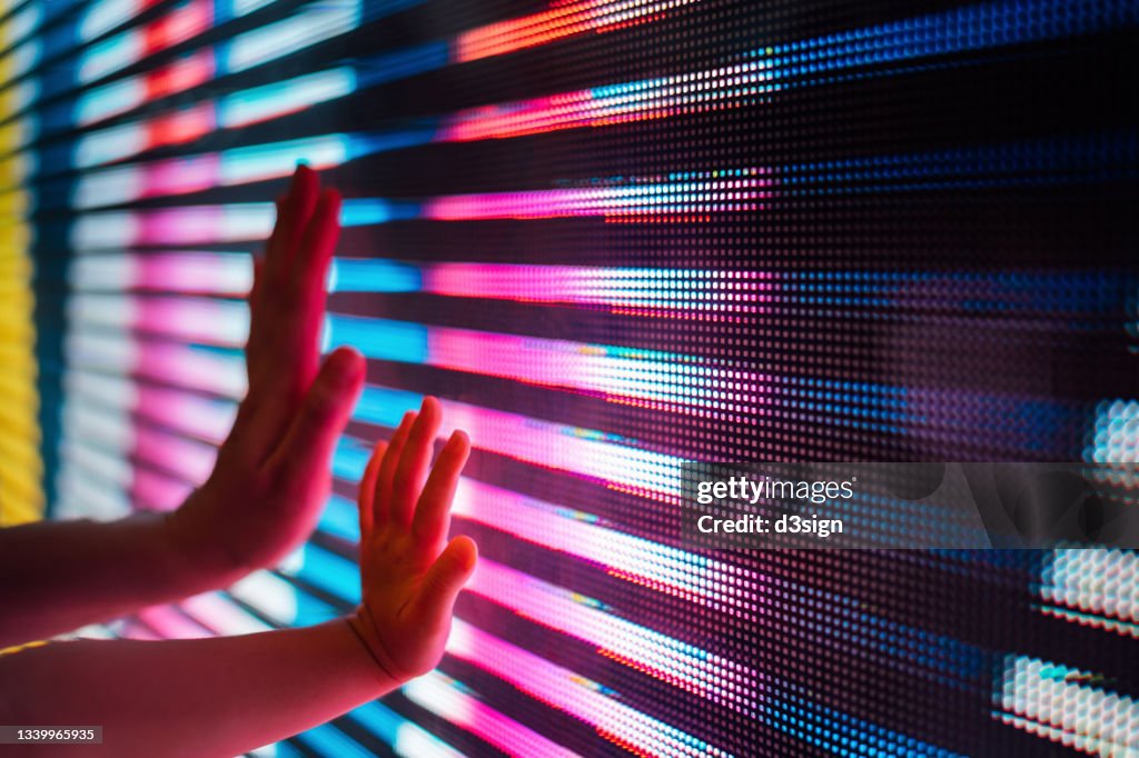 Close up of a mother and kid's hand touching illuminated and multi-coloured LED display screen, connecting to the future