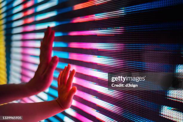 close up of a mother and kid's hand touching illuminated and multi-coloured led display screen, connecting to the future - breakthrough concept stock-fotos und bilder