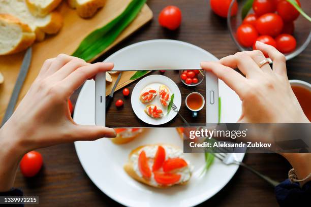 hands of a blogger girl with a phone close-up. a woman takes pictures of her breakfast. sandwiches, healthy organic farm products on a plate. the concept of cooking, hobbies, blogging in social networks. vegetarian and vegan food. top view. - mobile phone edit stockfoto's en -beelden