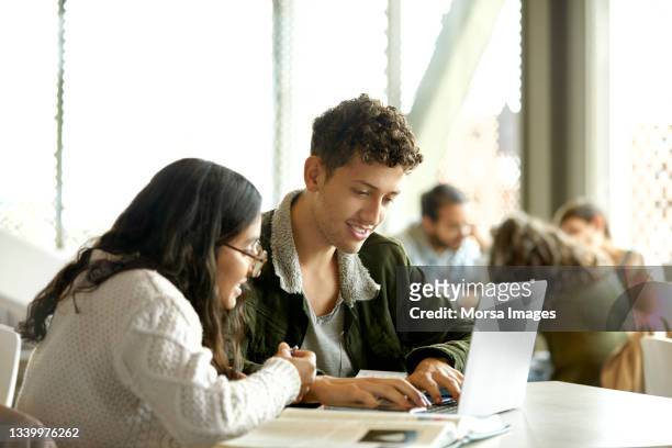 smiling students studying over laptop in cafeteria - student laptop stock-fotos und bilder