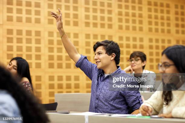 smiling student with hand raised in lecture hall - estudiantes universitarios bogota fotografías e imágenes de stock