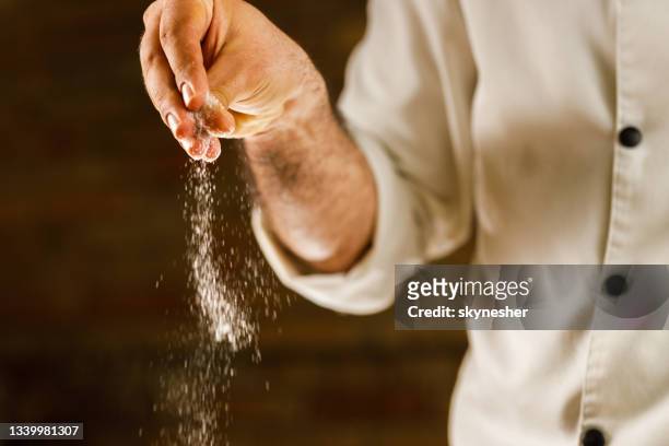 nahaufnahme eines kochs, der salz in sein rezept einfüge. - gesalzenes stock-fotos und bilder