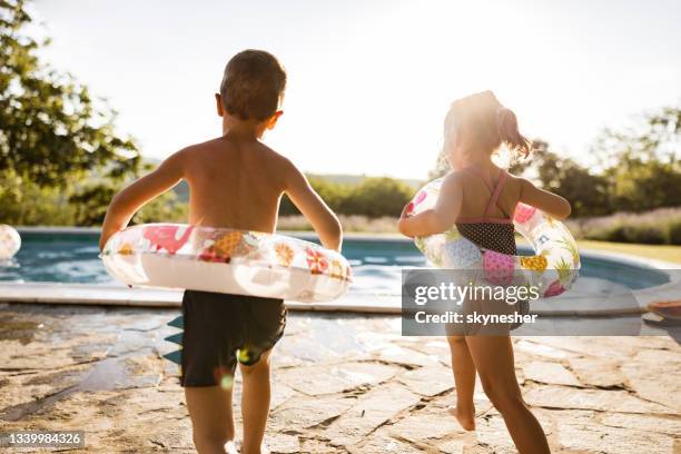 rear view of small kids running towards the pool in the backyard. - boy-with-a-girl-playing-at-the-poolside stock pictures, royalty-free photos & images