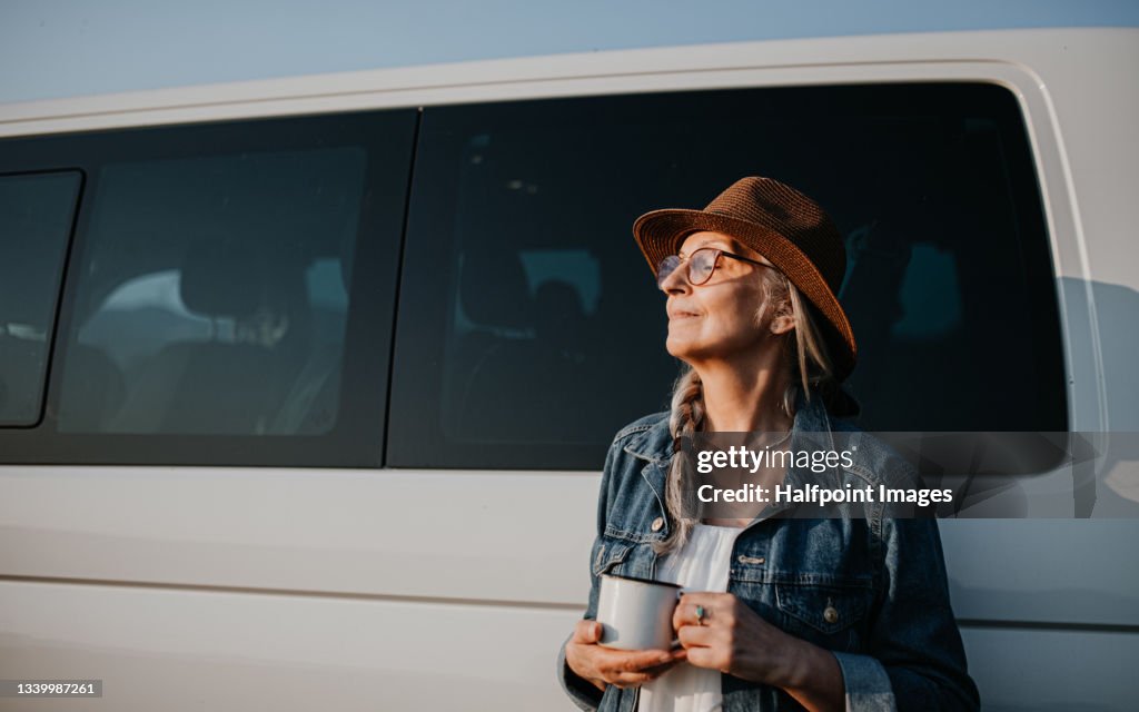 Senior woman resting outdoors at sunset, caravan trip holiday.