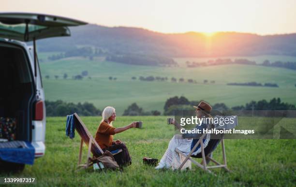 senior women friends eating and sitting by car boot outdoors at sunset, caravan trip holiday. - female with friend in coffee stock pictures, royalty-free photos & images