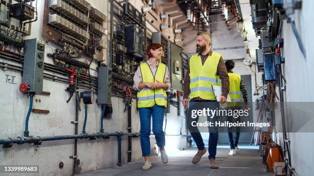 low angle view of male and female control engineers checking electrical operating system at control room indoors in power station, walking and talking. - man walking low angle stock pictures, royalty-free photos & images