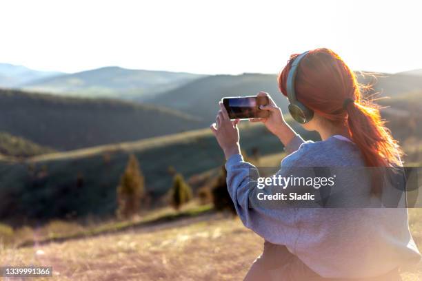 eine junge frau, die den sonnenuntergang vom berggipfel genießt - fotografieren stock-fotos und bilder