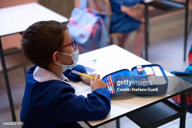 Child wears a protective mask inside an elementary school classroom with separate desks for social distancing measures to prevent COVID 19 inside on...