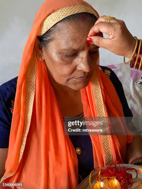 close-up image of indian, hindu woman, wearing sari traditional clothing, being anointed with sindoor (red cosmetic powder) on forehead as part of raksha bandhan hindu festival of brotherhood and love, headshot portrait - woman in red sari stock pictures, royalty-free photos & images