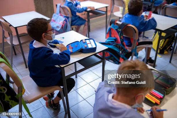 Children wear protective masks inside an elementary school classroom with separate desks for social distancing measures to prevent COVID 19 inside on...