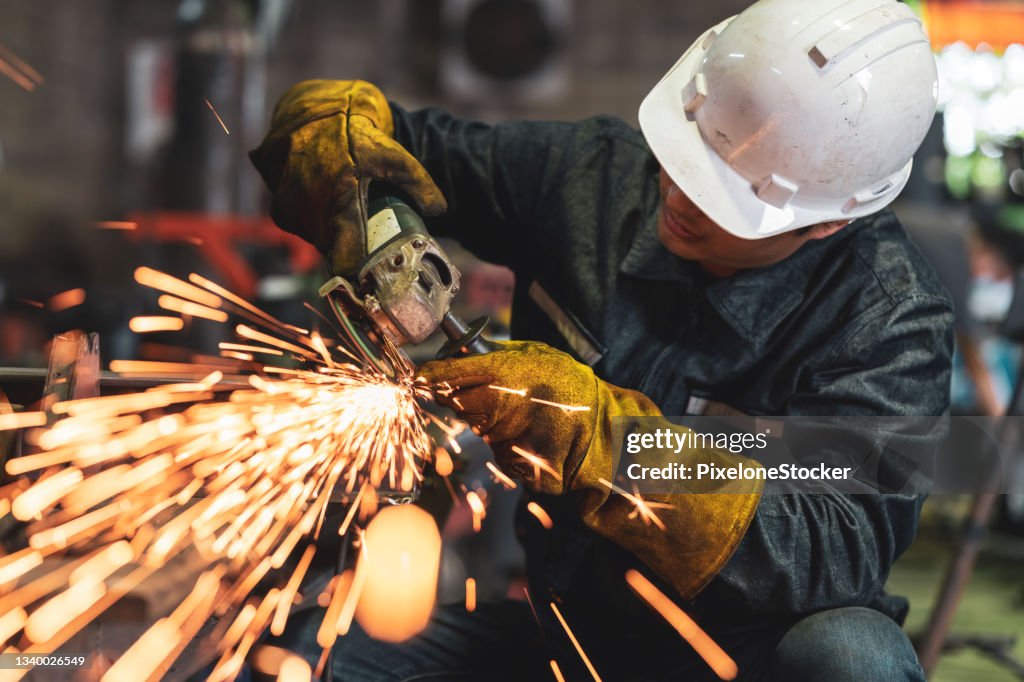 Man worker using grinder to polish the metal surface in the workshop.