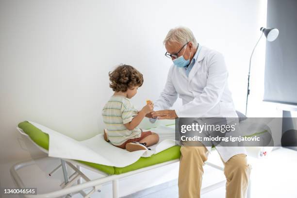 médecin parlant avec un petit garçon alors qu’ils sont assis sur une table d’examen dans le bureau du pédiatre - table dexamen médical photos et images de collection