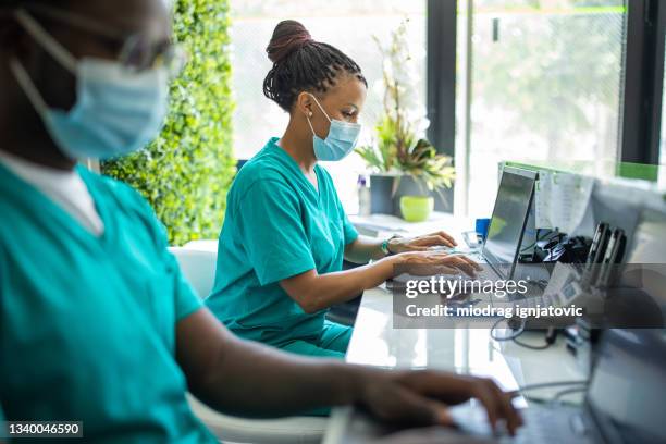 krankenschwester mit schutzmaske, die am laptop am empfang der medizinischen klinik arbeitet - schwesterntisch stock-fotos und bilder