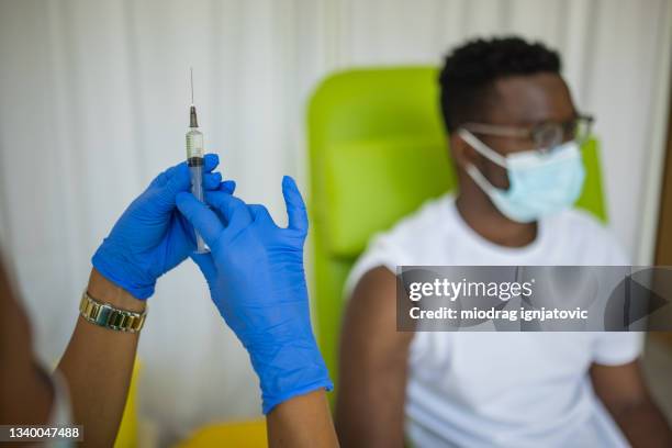 nurse preparing to vaccinate young man with vaccine against covid-19 - immunology stock pictures, royalty-free photos & images