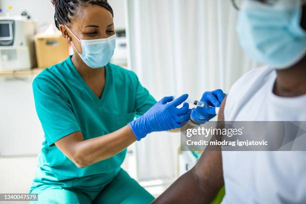 healthcare worker injecting vaccine against covid-19 to young man - global health stock pictures, royalty-free photos & images