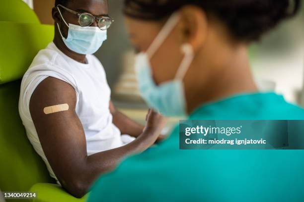 young man with adhesive bandage after vaccination against covid-19 at medical clinic - bandage stock pictures, royalty-free photos & images