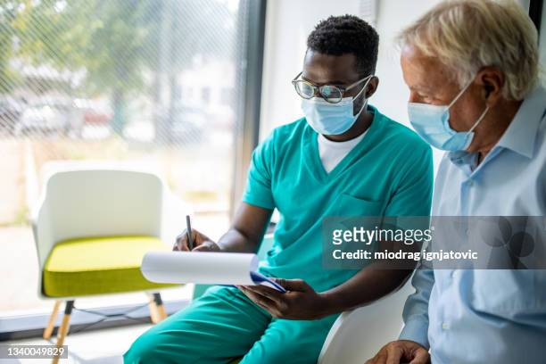 männliche krankenschwester bei einem gespräch mit einem älteren patienten in der medizinischen klinik - arbeiten pflege senior stock-fotos und bilder