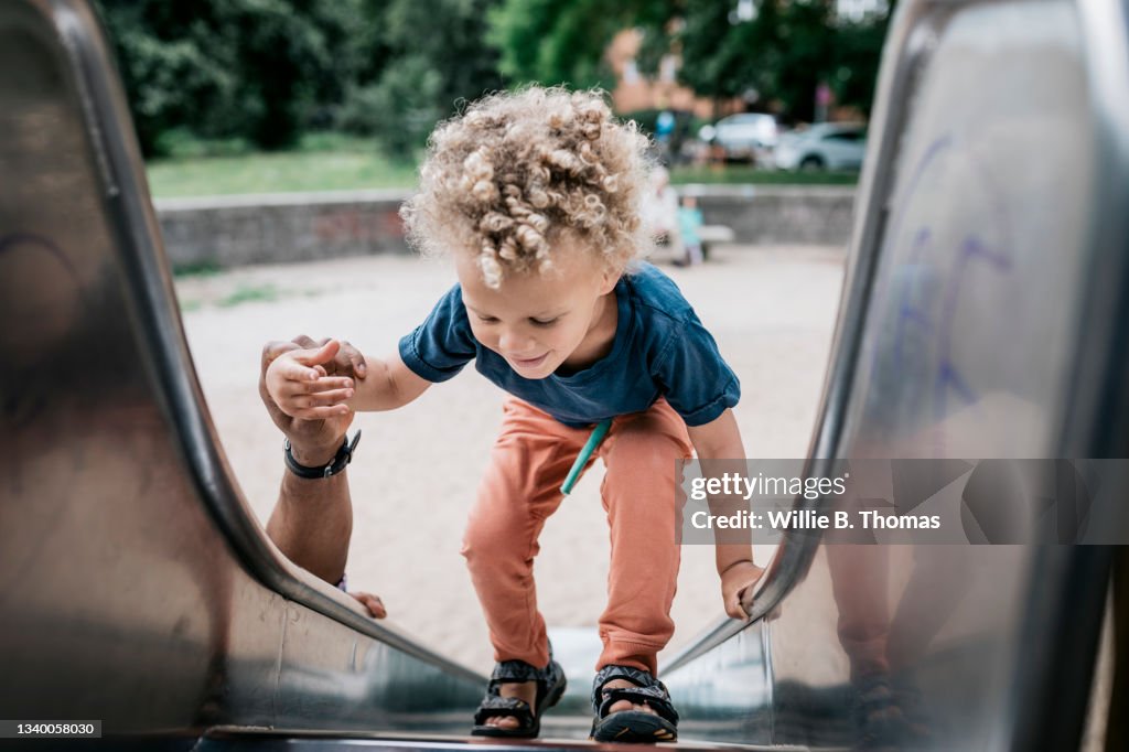 Young Boy Walking Up Slide With Help From Granddad