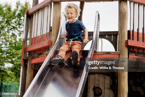 young boy going down slide in playground - sliding stock-fotos und bilder