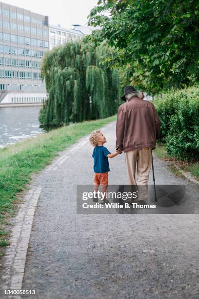 young boy holding grandfather's hand while out walking - hand holding stick stock pictures, royalty-free photos & images