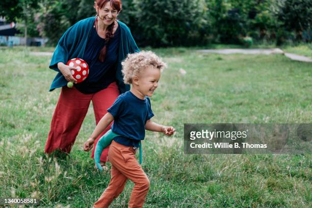 young boy running in park with grandmother - oma und enkel stock-fotos und bilder
