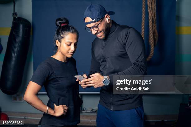 woman and personal trainer making exercise plan on smartphone in gym. - personal trainer stock pictures, royalty-free photos & images