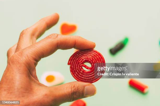 closeup of woman's hand holding a red liquorice spiral jelly bean, with background of different jelly beans - licorice stock pictures, royalty-free photos & images