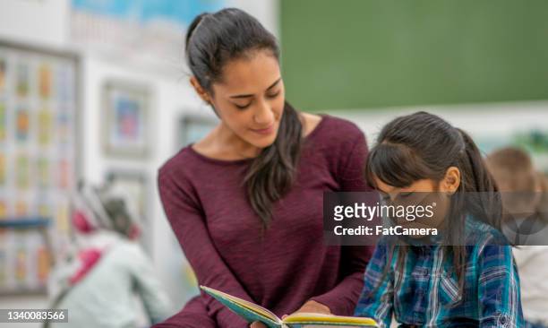female preschool teacher helping a student read in a classroom - spanish and portuguese ethnicity stock pictures, royalty-free photos & images