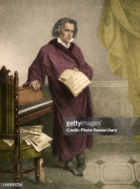 Colorized illustration depicts Ludwig van Beethoven as he leans on a spinet, pages of sheet music in his hand, circa 1870.