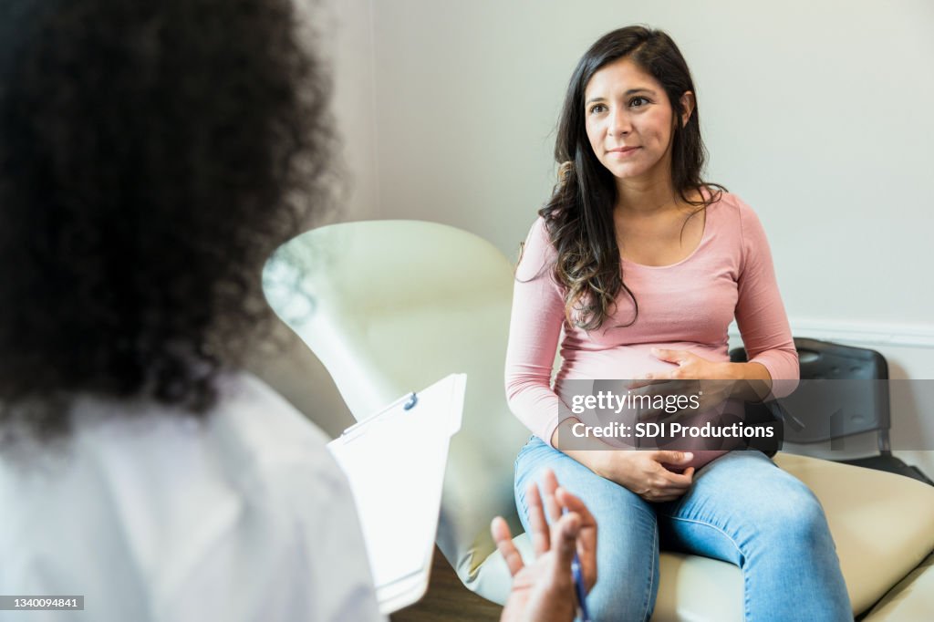 La futura madre toca el abdomen mientras escucha al médico irreconocible