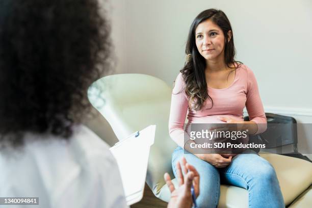 expectant mother touches abdomen while listening to unrecognizable doctor - prenatal care stock pictures, royalty-free photos & images