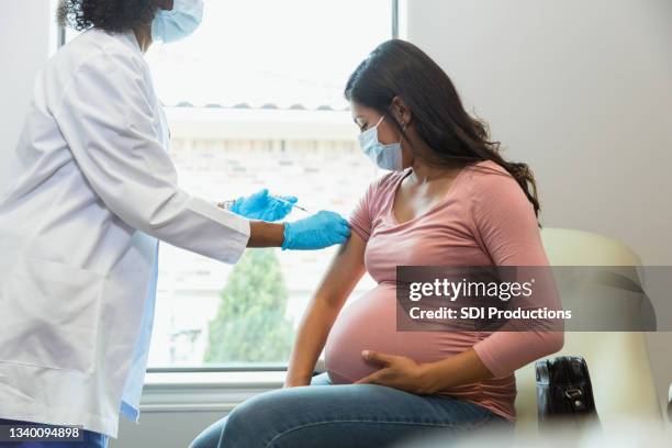 futura madre observa cómo la tecnología le da la vacuna - vacunas fotografías e imágenes de stock