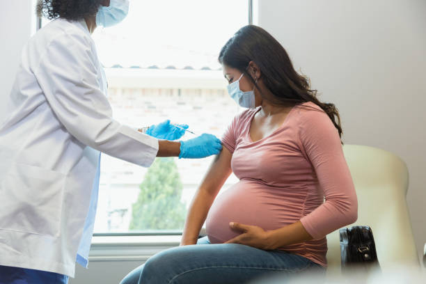 expectant mother watches as tech gives her vaccine - baby vaccination stock pictures, royalty-free photos & images
