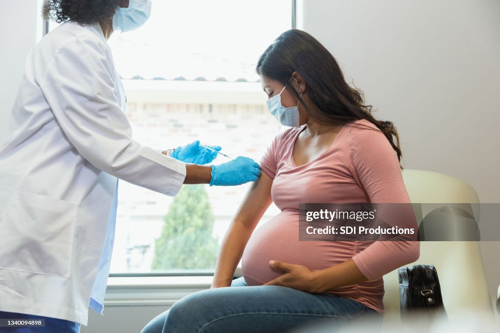 Expectant mother watches as tech gives her vaccine