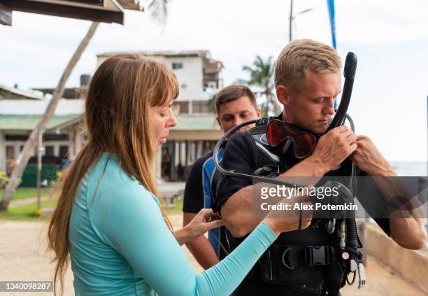 young woman and man are helping to a team member to adjust aqualung before diving expedition. - aqualung diving equipment stockfoto's en -beelden