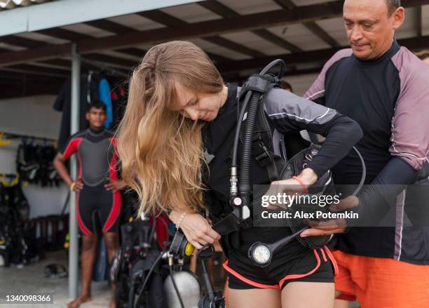 mature man helps a young woman to adjust underwater equipment and aqualung before diving trip. - aqualung diving equipment stockfoto's en -beelden