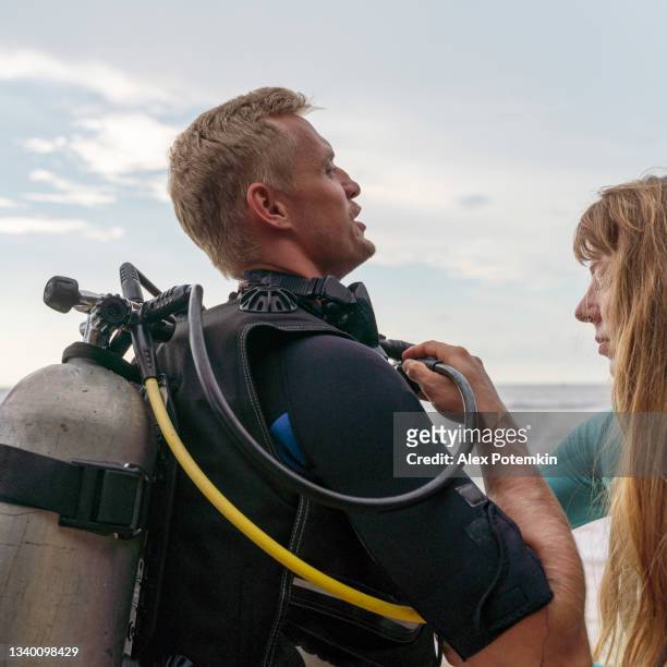 una mujer joven ayudando a un hombre a ajustar aqualung antes de bucear. - aqualung diving equipment fotografías e imágenes de stock